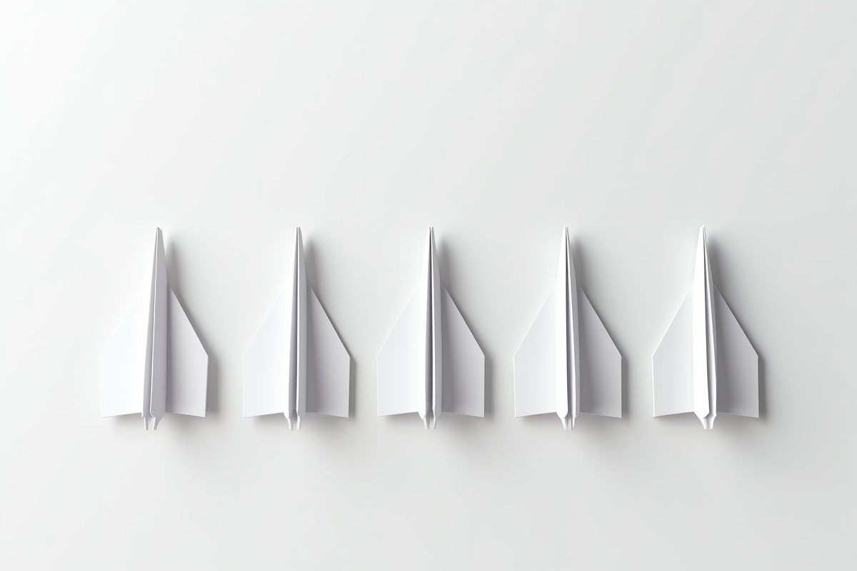 Plusieurs avions en papier alignes sur une surface blanche